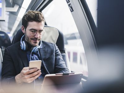 Man on train with headphones, phone, and laptop