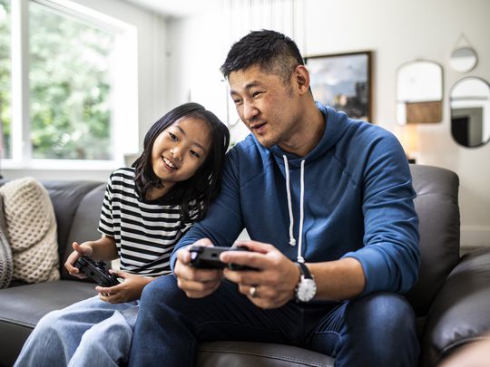 Two people (one adult, one kid) playing video games on the couch.