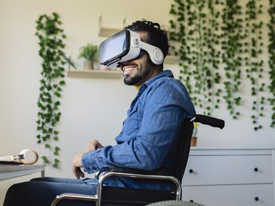 Someone in a wheel chair sitting at a desk wearing a virtual reality headset. 