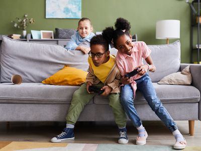 Kids playing video games at home together and fighting playfully.