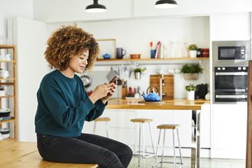 A woman sitting in her kitchen smiling at her smartphone