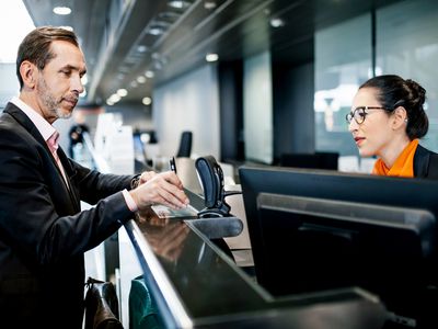 A businessman using a mobile boarding pass to check in at an airline desk in an airport.