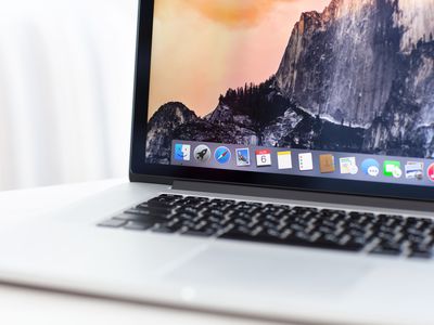 A Macbook Pro is open with on a white table, with a background of mountains on the screen.