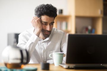 A man is working on a laptop computer looking frustrated.