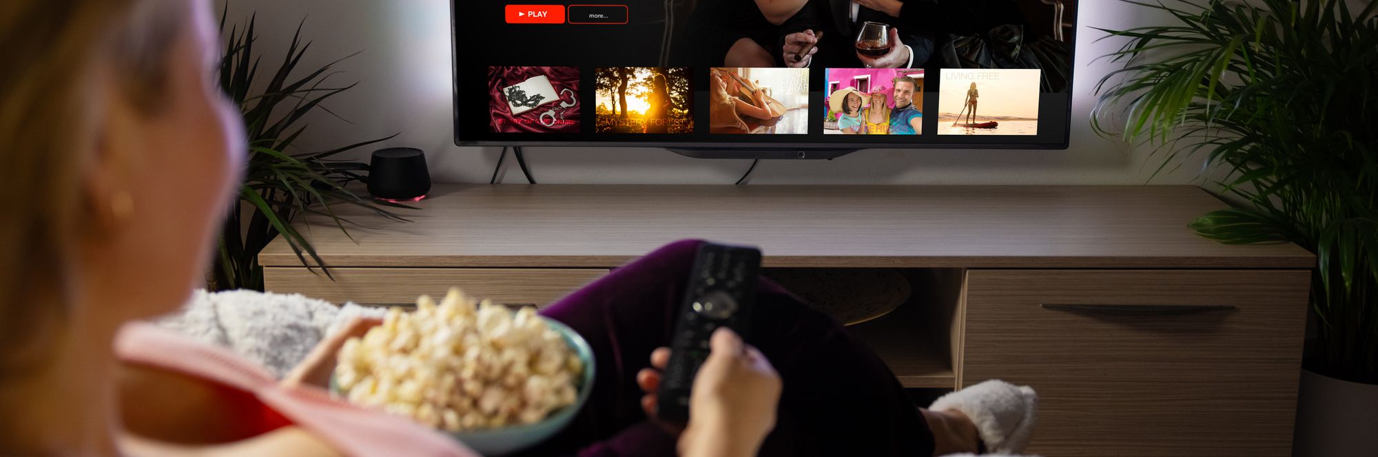 Woman holding popcorn using streaming remote to watch TV.