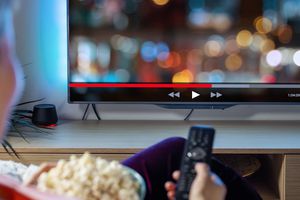 Woman streaming shows on TV with popcorn and remote in hand